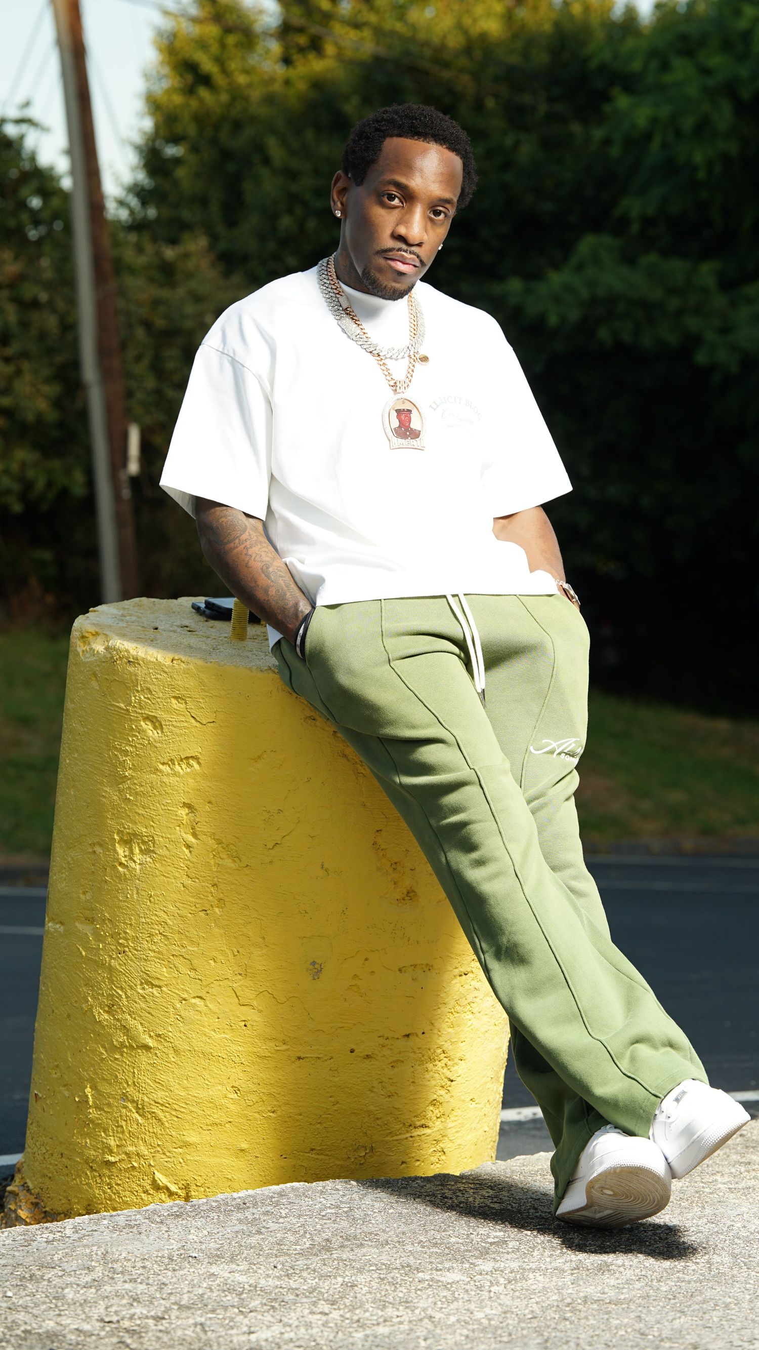 A person in a white t-shirt and mint green pants sits casually against a yellow concrete barrier outdoors.