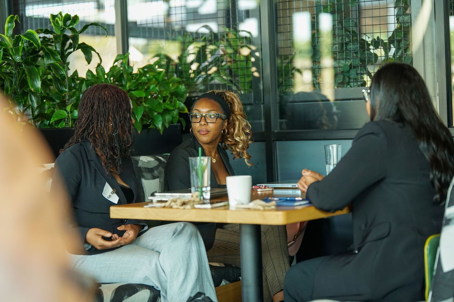 Three professional women engaged in conversation at a table during a business networking event.