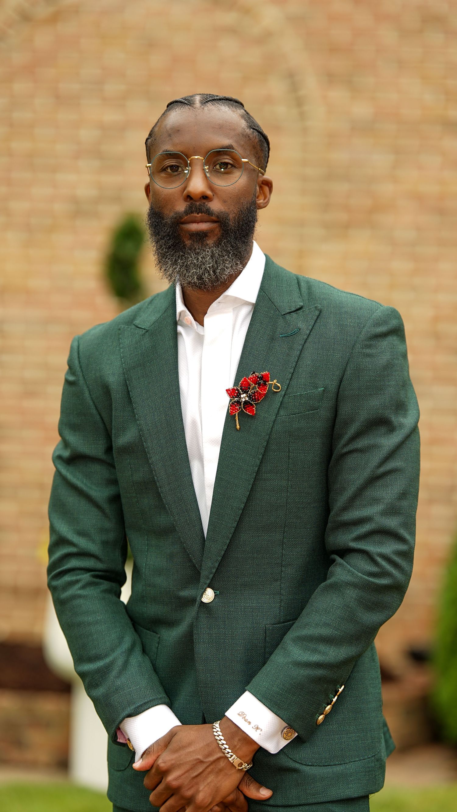 Dapper gentleman in green blazer with red boutonniere poses against brick wall background.