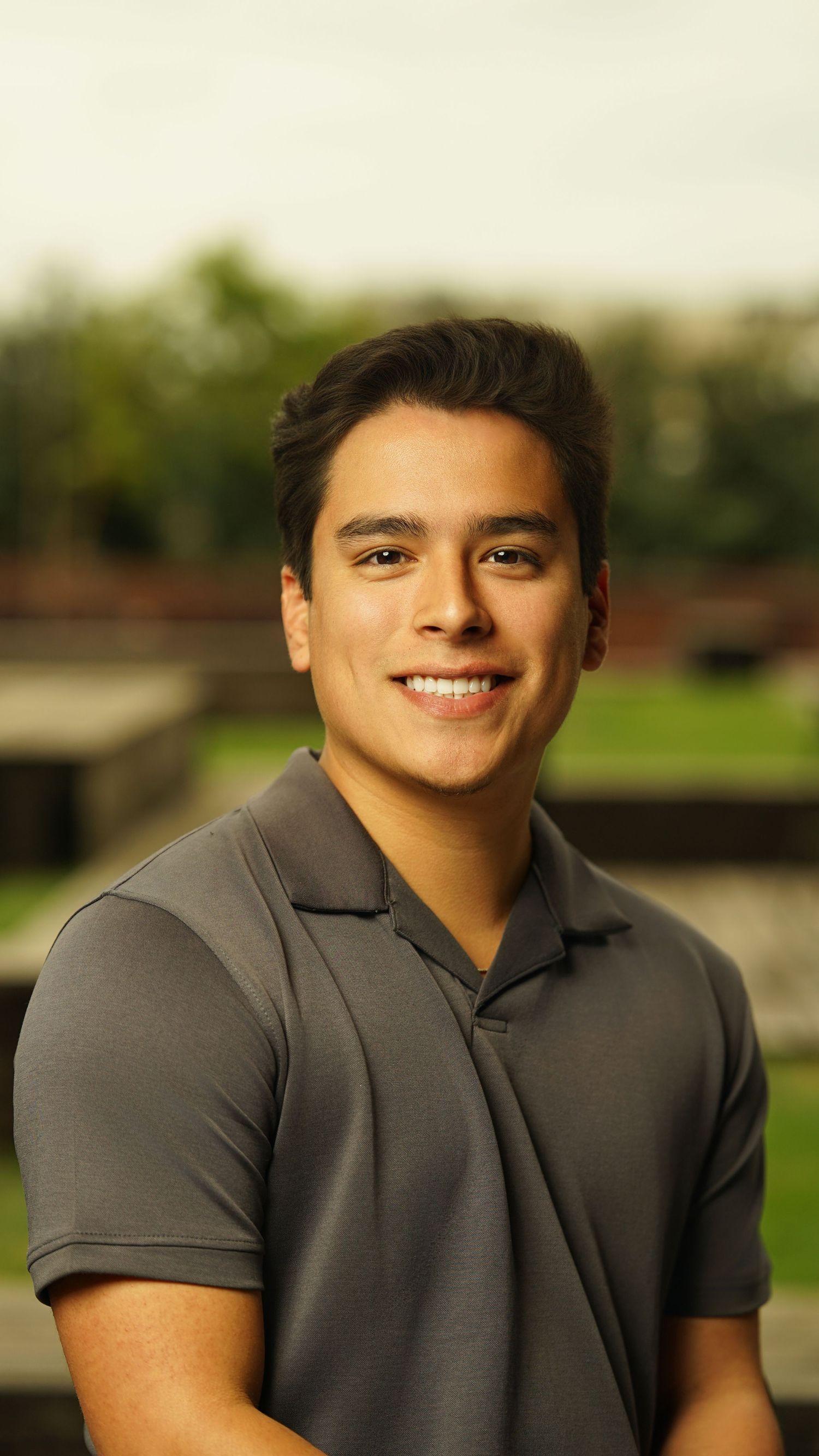 Casual headshot of person in grey polo shirt smiling against natural background.