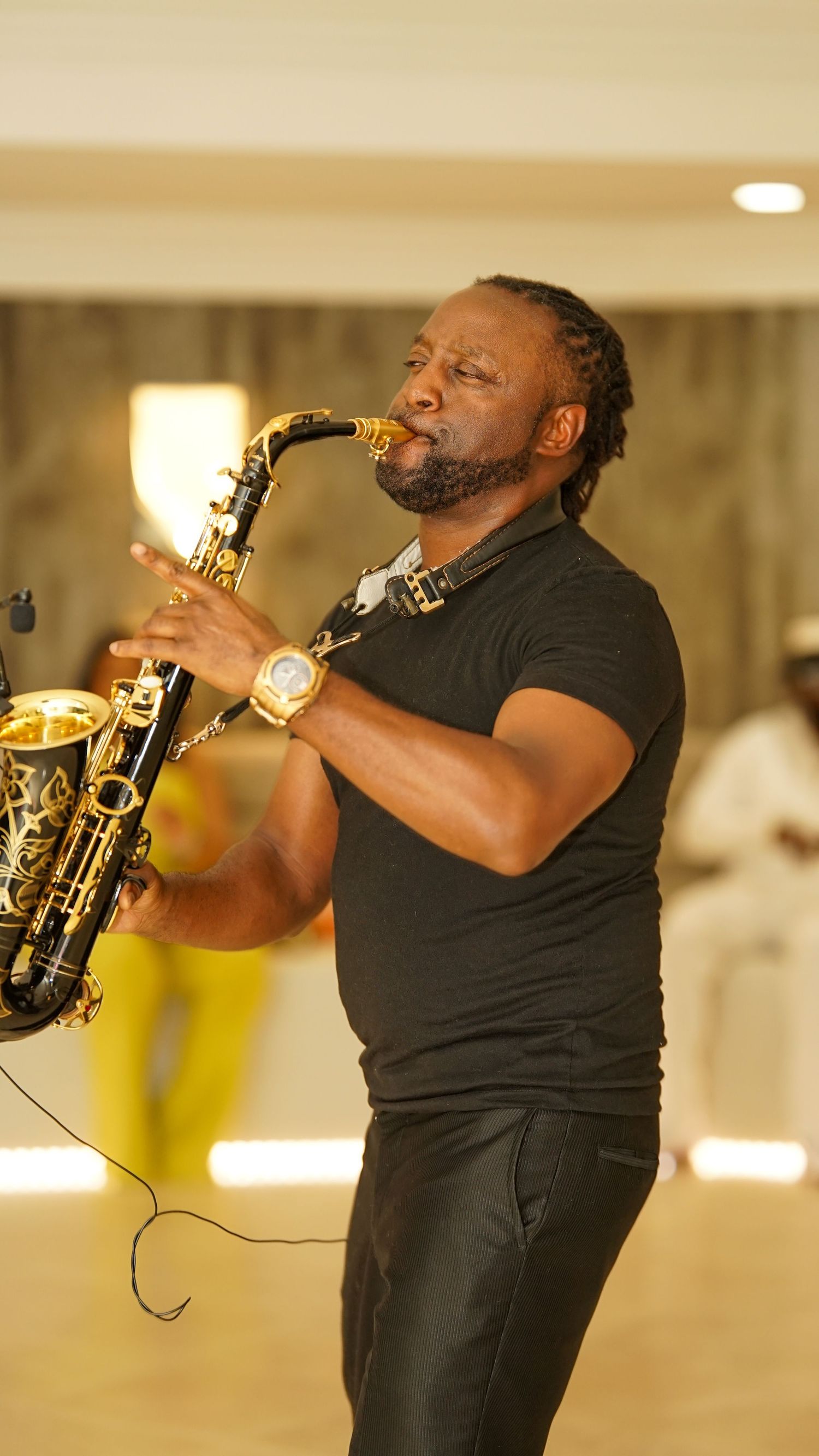 Musician performing passionately on saxophone in black attire under indoor lighting.