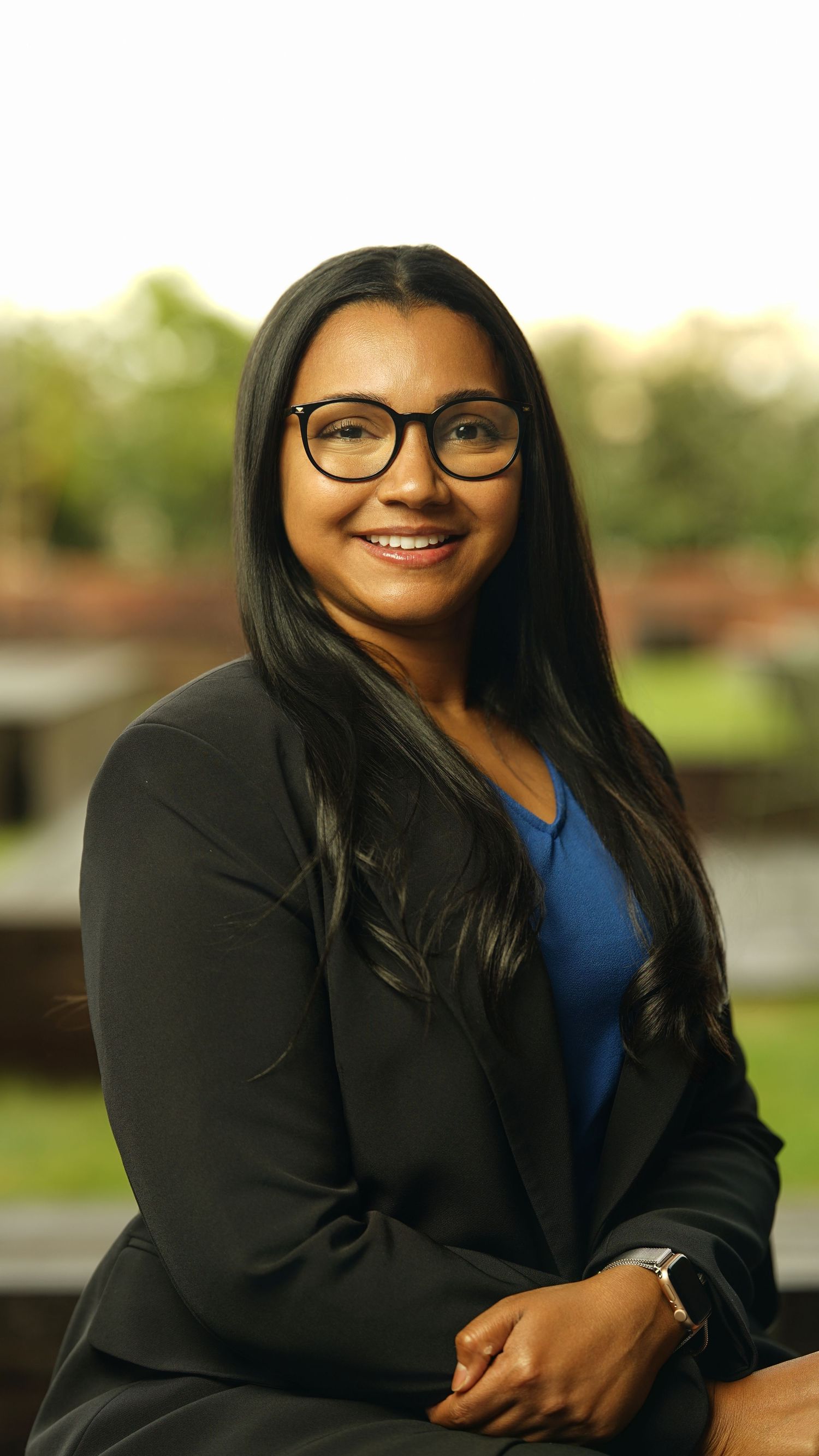 Professional portraits featuring someone in glasses, a blue top, and black blazer outdoors.