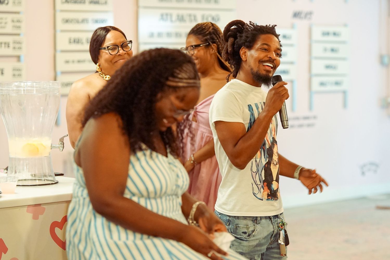 Group of people laughing and having fun at an indoor event, one holding a microphone.