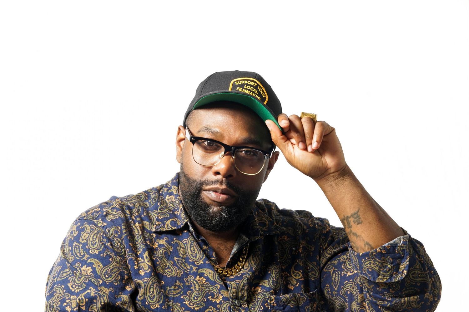 Man in floral shirt and green cap posing confidently against white background.