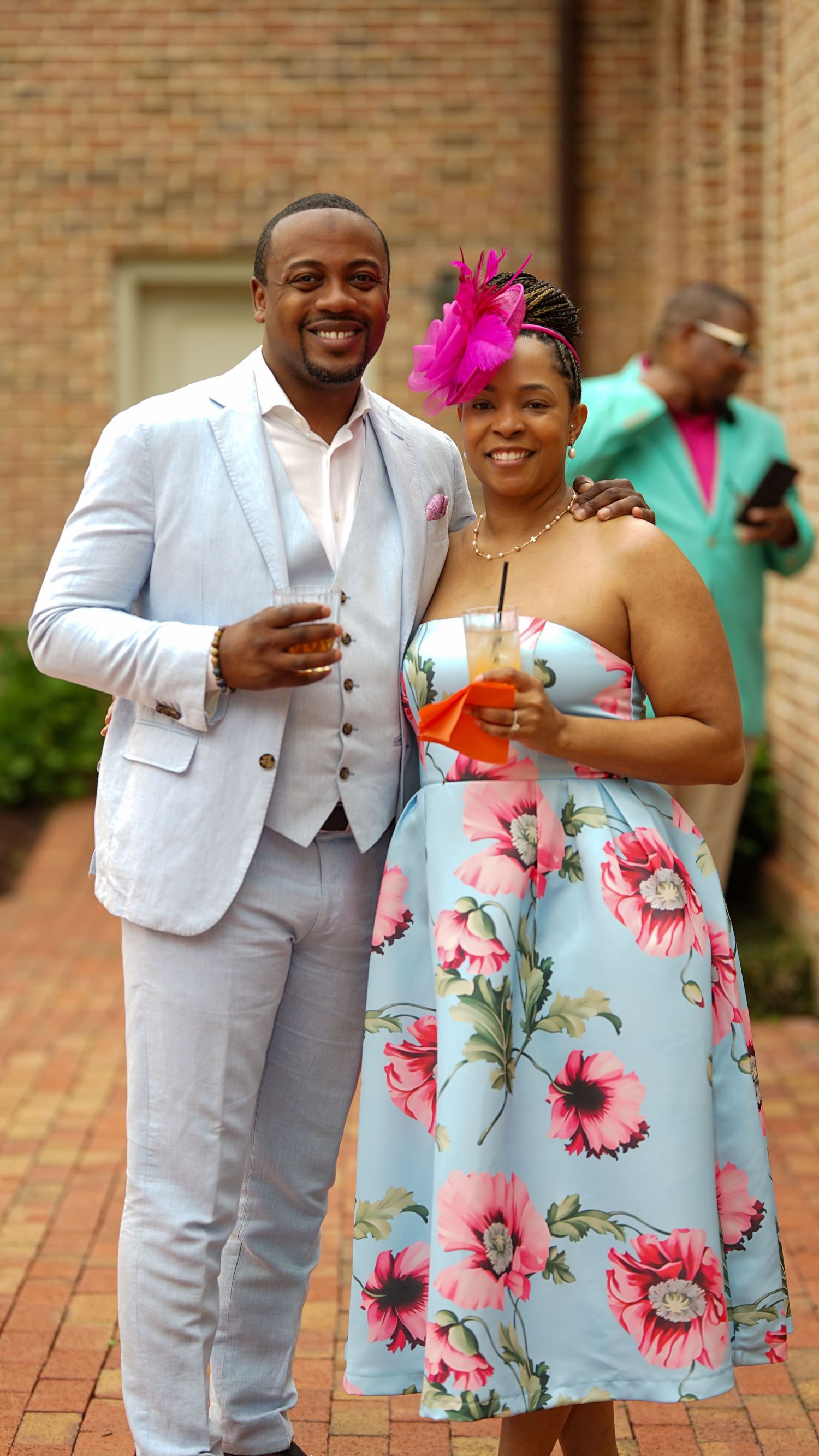 Couple in coordinated formal wear with floral dress and light colored suit on brick patio.