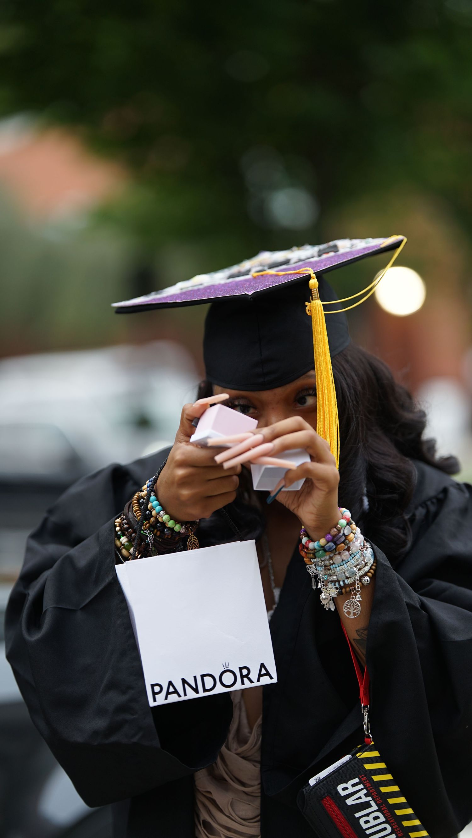 Graduate examines contents of Pandora envelope while wearing graduation attire.