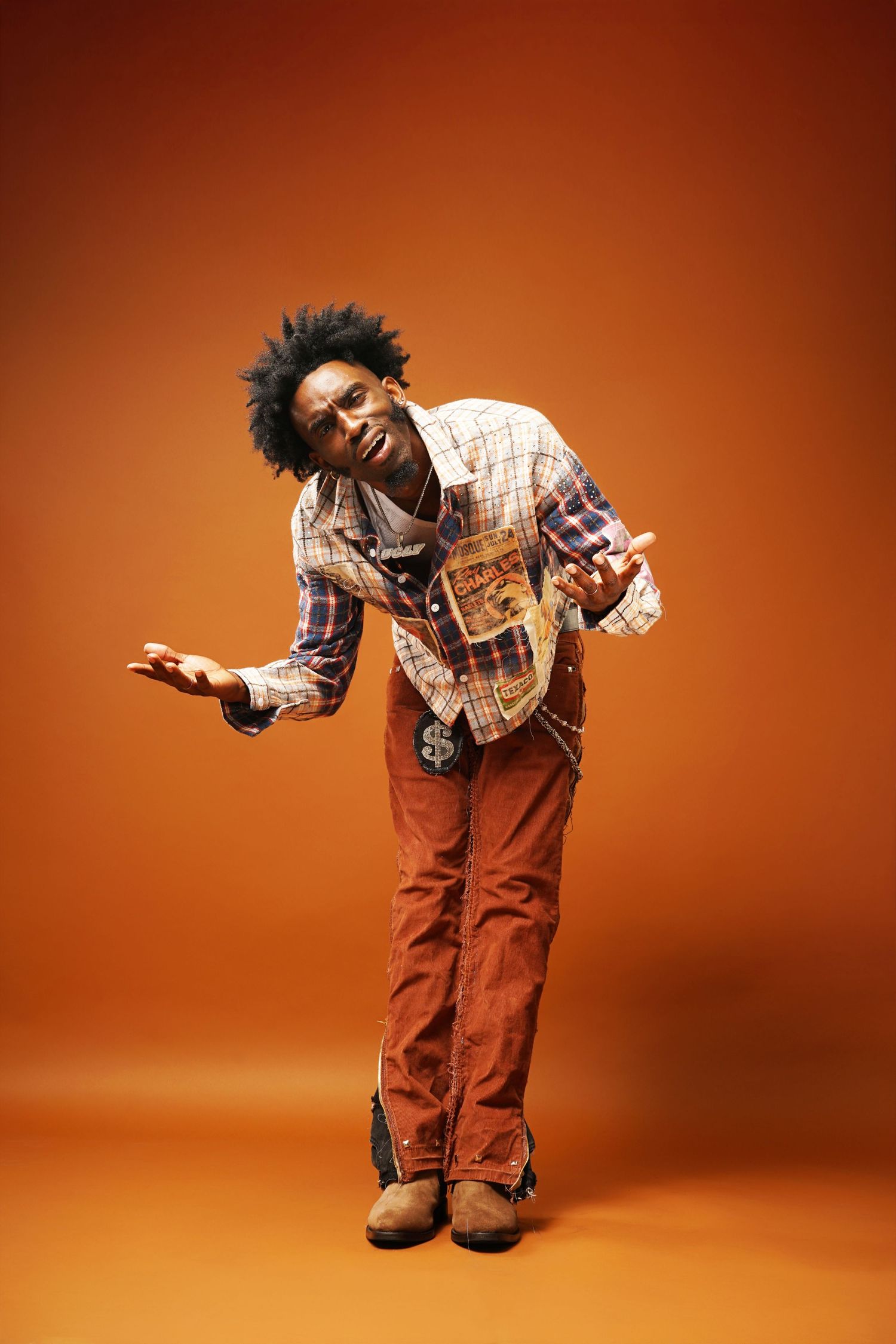 Dynamic pose showing movement in plaid patchwork jacket against orange backdrop.