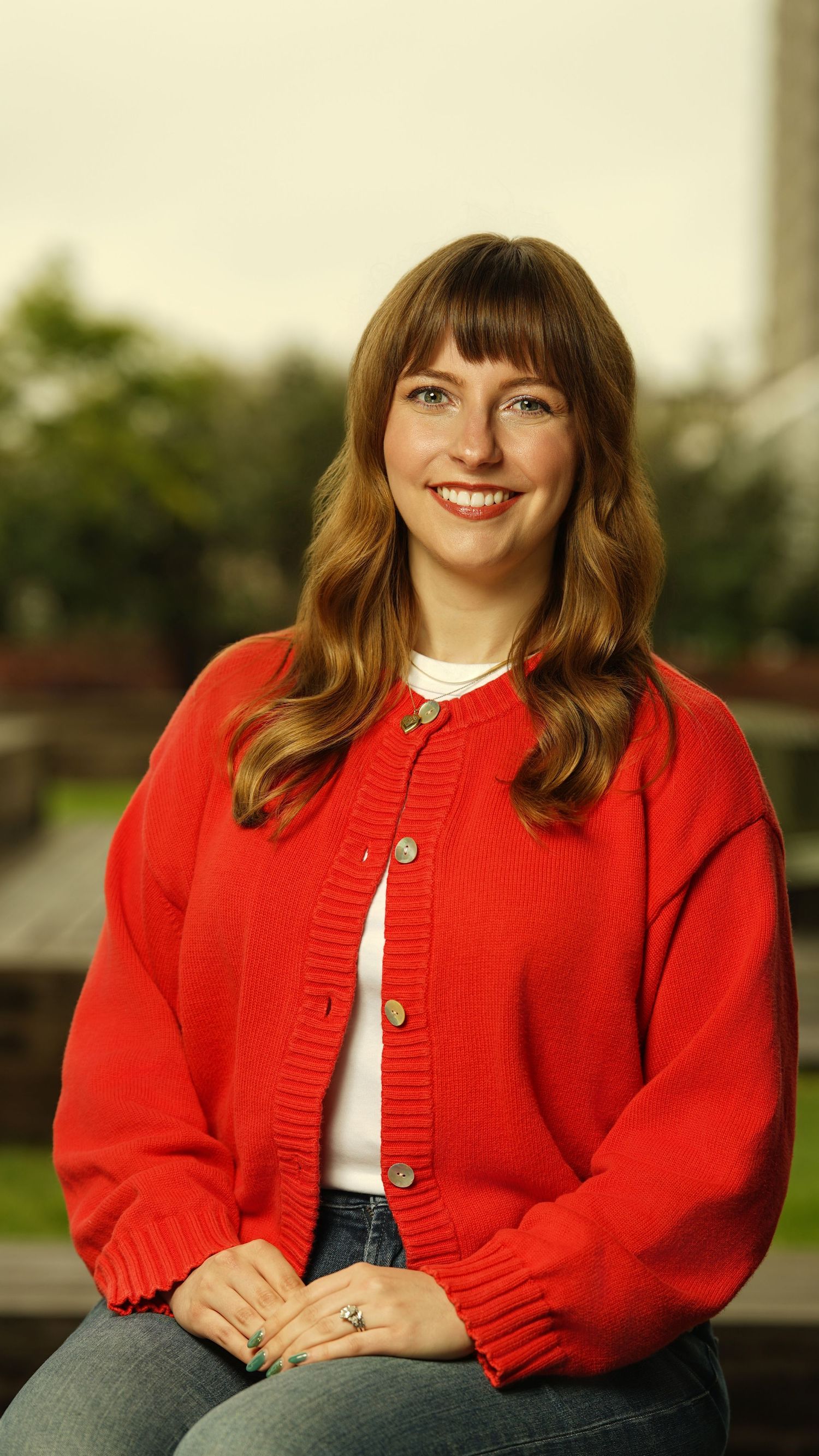 Person wearing a bright red cardigan and white top poses casually outdoors.
