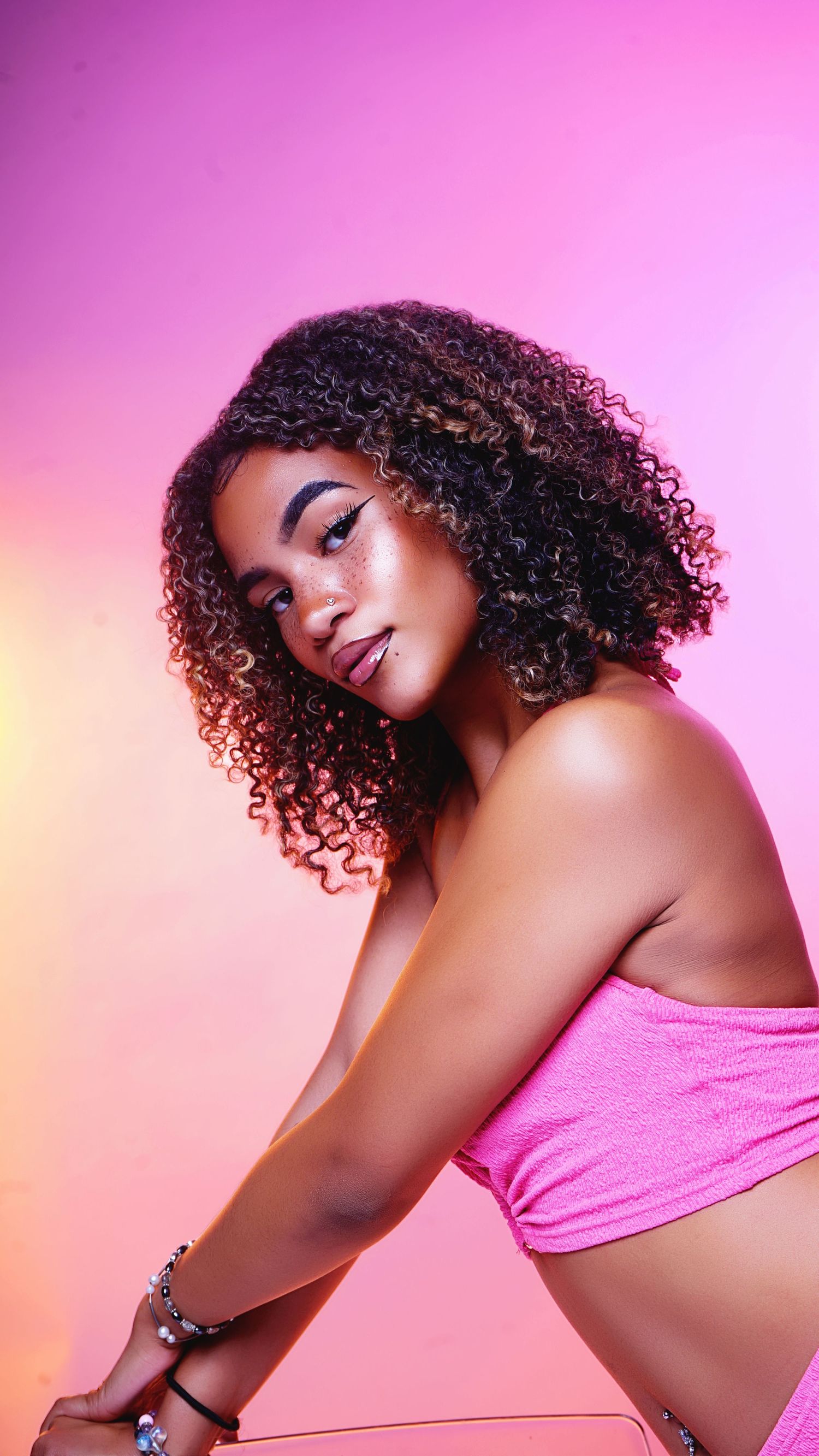 Beauty portrait with curly hair against pink gradient background wearing pink top.
