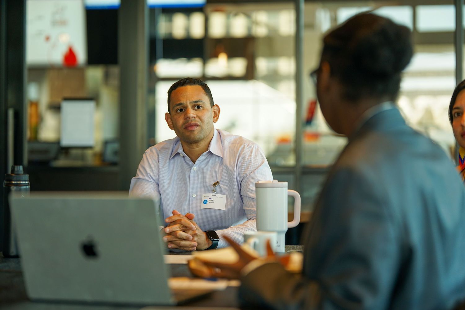 Professional man in white shirt listening attentively during a business meeting with a laptop and coffee mug.