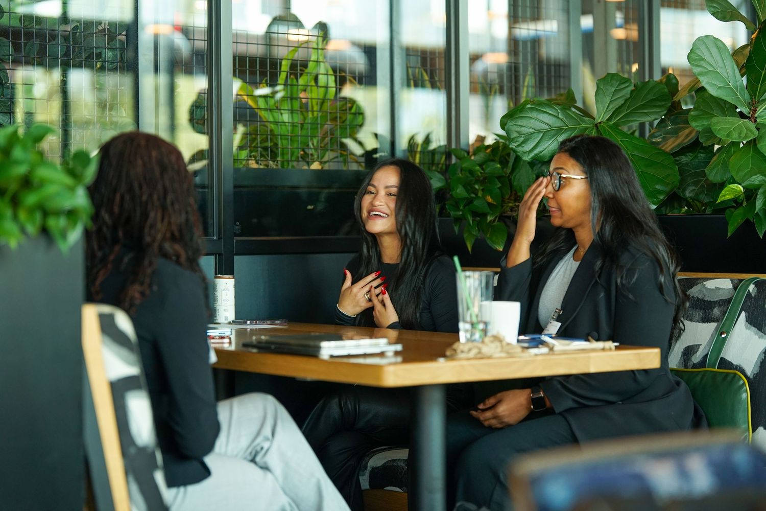 Three professional women laughing and networking at a cafe table with drinks.