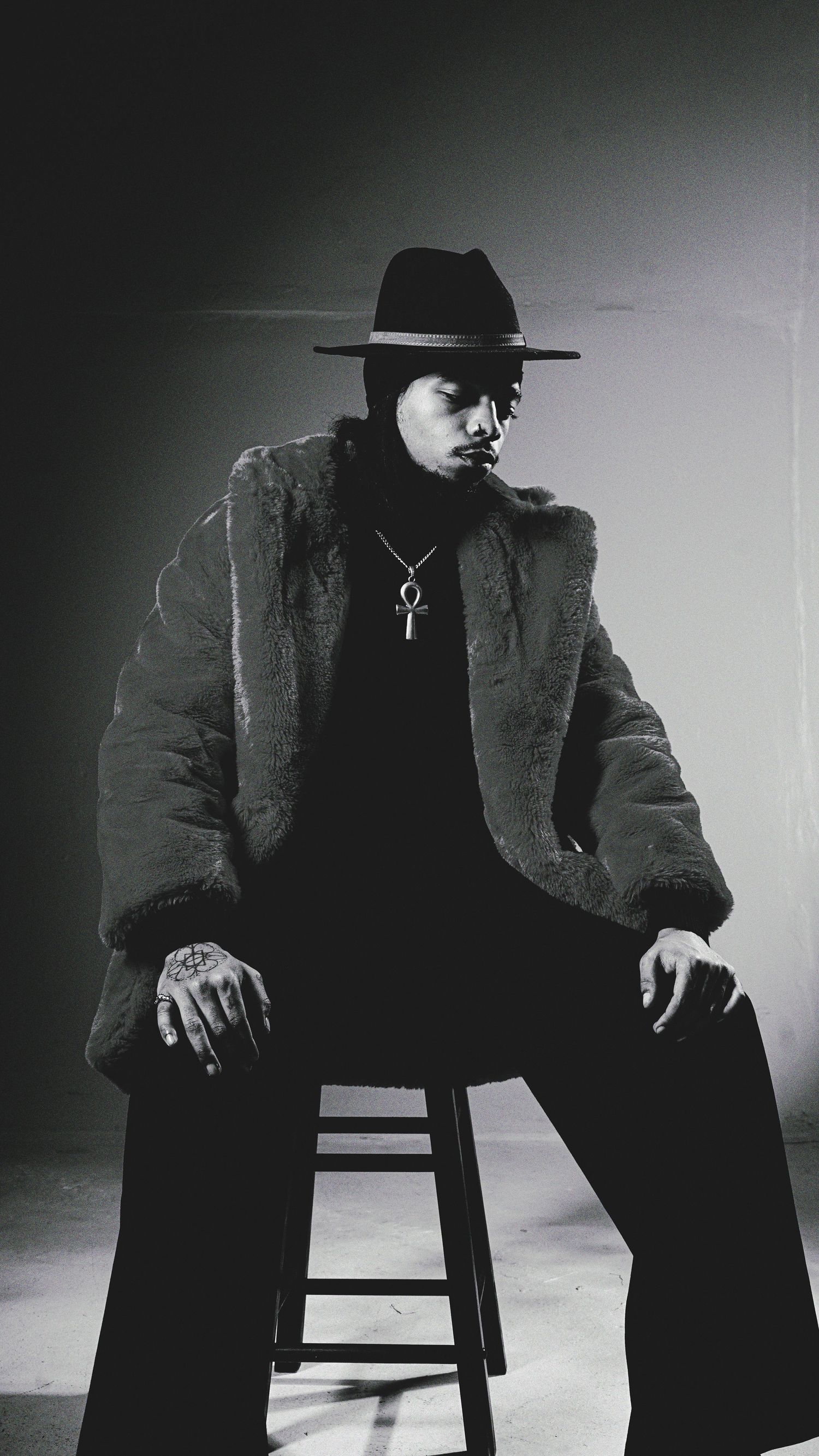 Dramatic noir-style portraits of a figure in fedora and coat seated on a wooden stool.