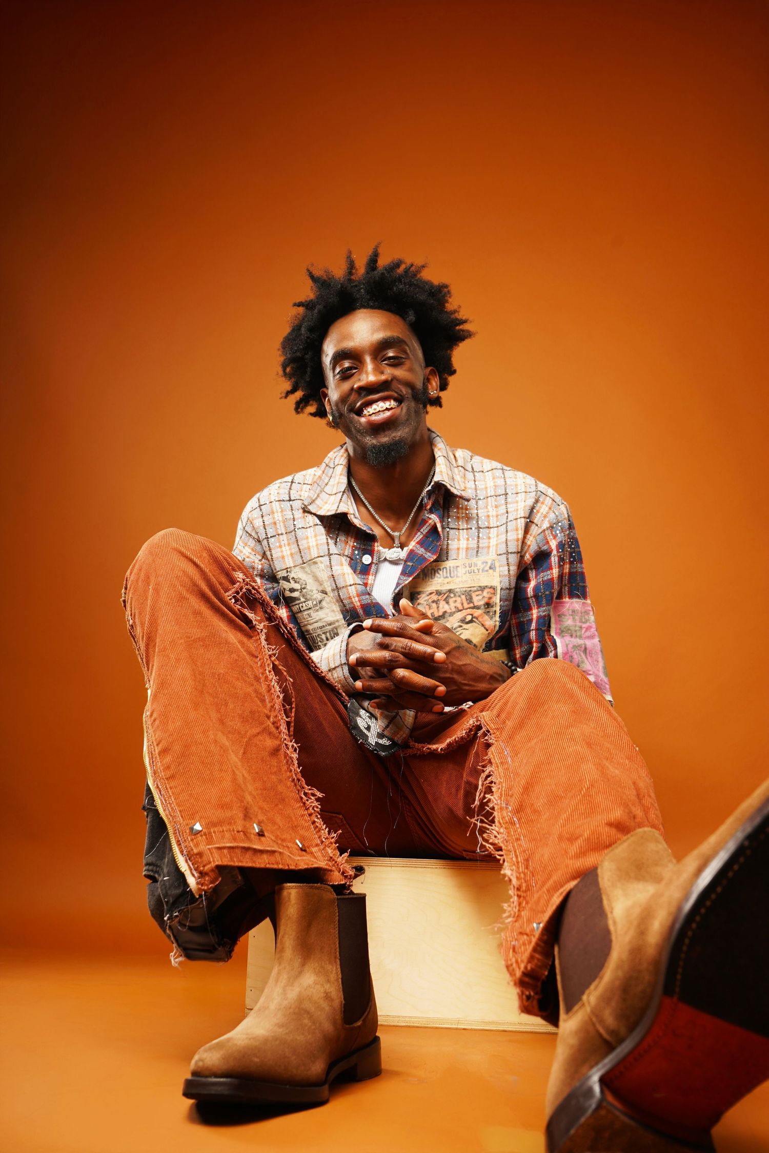 Joyful portrait sitting on cube wearing distressed denim and patchwork jacket.
