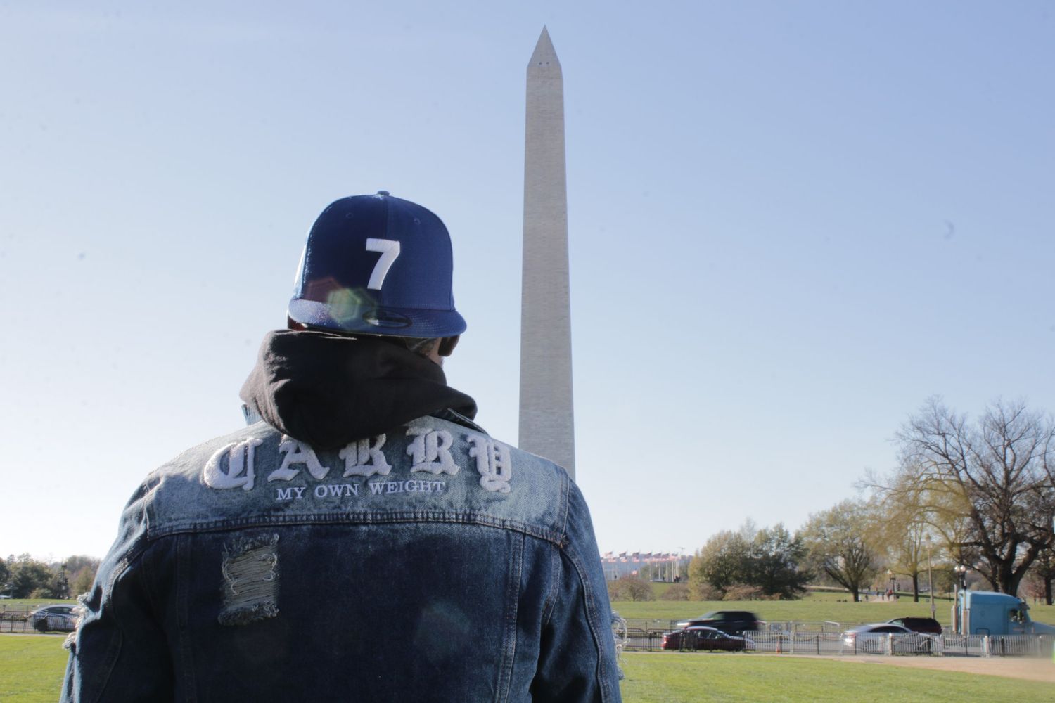 Person in denim jacket and blue snapback views Washington Monument on clear day.