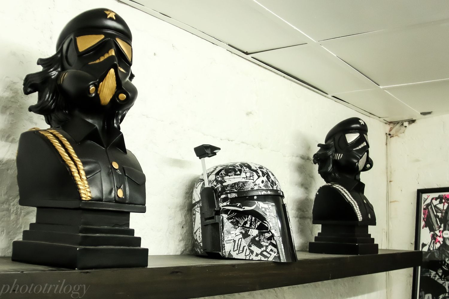 Three Star Wars themed bust sculptures displayed on a shelf, featuring TIE Fighter pilot and Boba Fett helmets in black and gold.