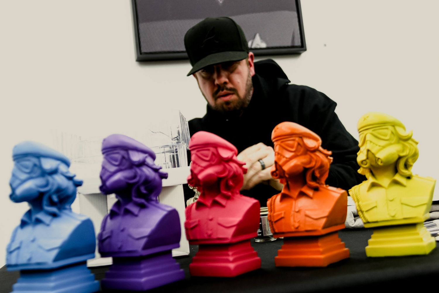 Artist arranging colorful cartoon bust sculptures in purple, pink, orange, and yellow on a black table.