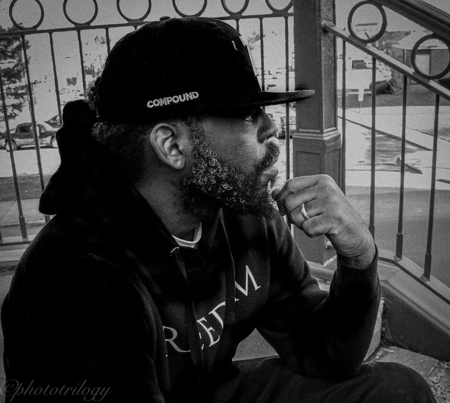 Black and white portrait of bearded man in cap sitting on porch steps.