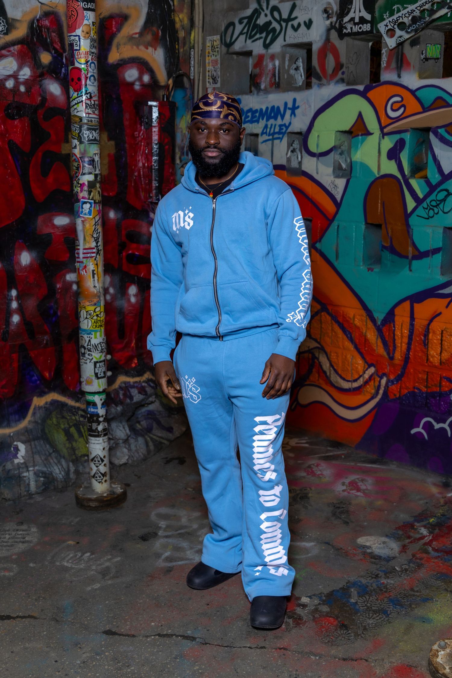 Athletic tracksuit in powder blue with white lettering shown against urban graffiti background.