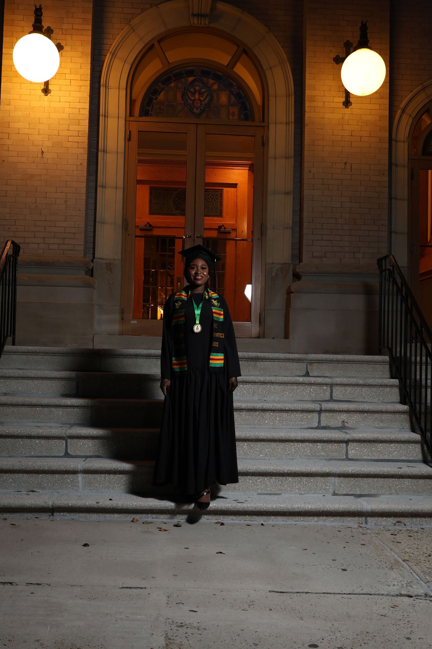 Nighttime graduation portrait on stone steps with illuminated archway.