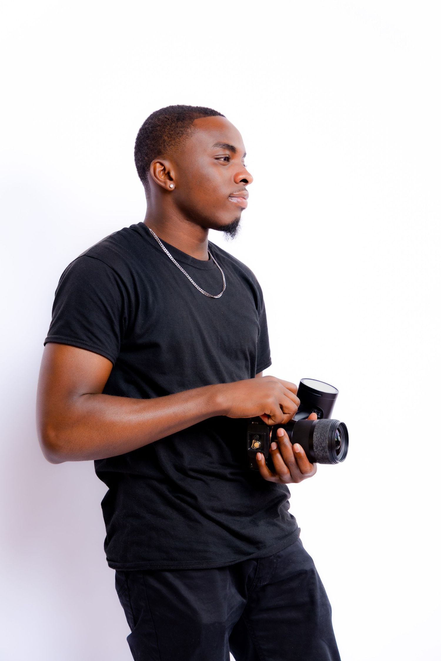 Photographer in black t-shirt holds professional camera against white background.