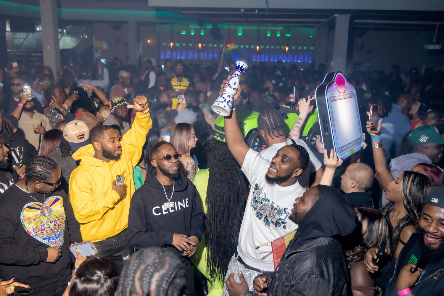 Crowded nightclub scene with energetic partygoers dancing and holding drinks in the air.