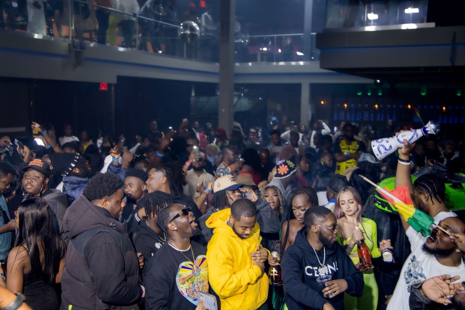 Packed nightclub dance floor with party guests dancing under blue lighting.