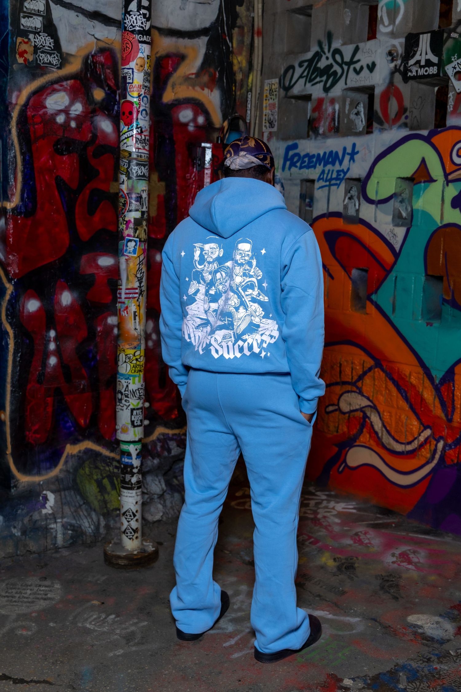 Person wearing a bright blue tracksuit with graphic design stands against colorful graffiti wall.