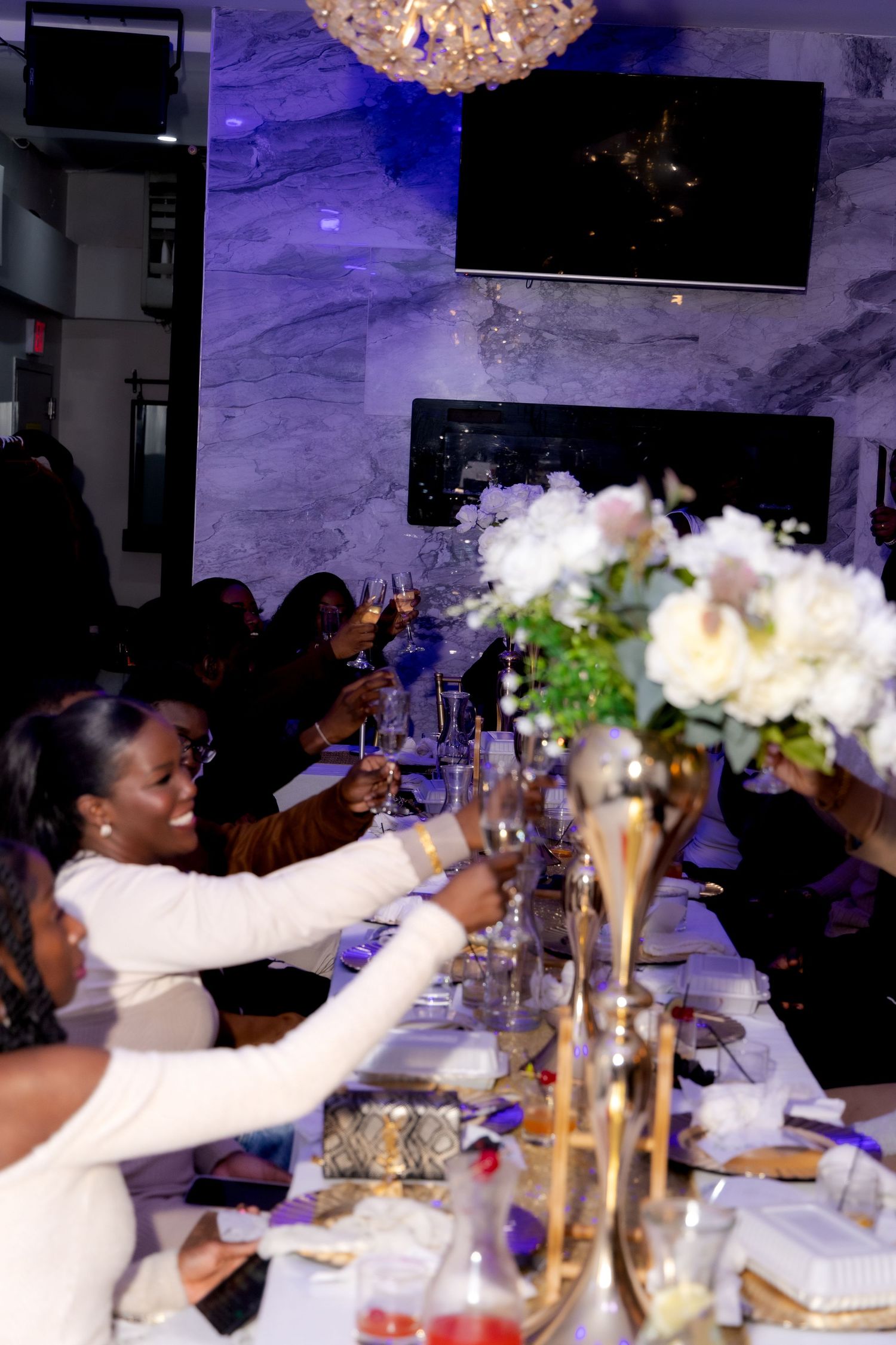 Dinner guests raising glasses in a toast at an elegant celebration with purple ambient lighting.