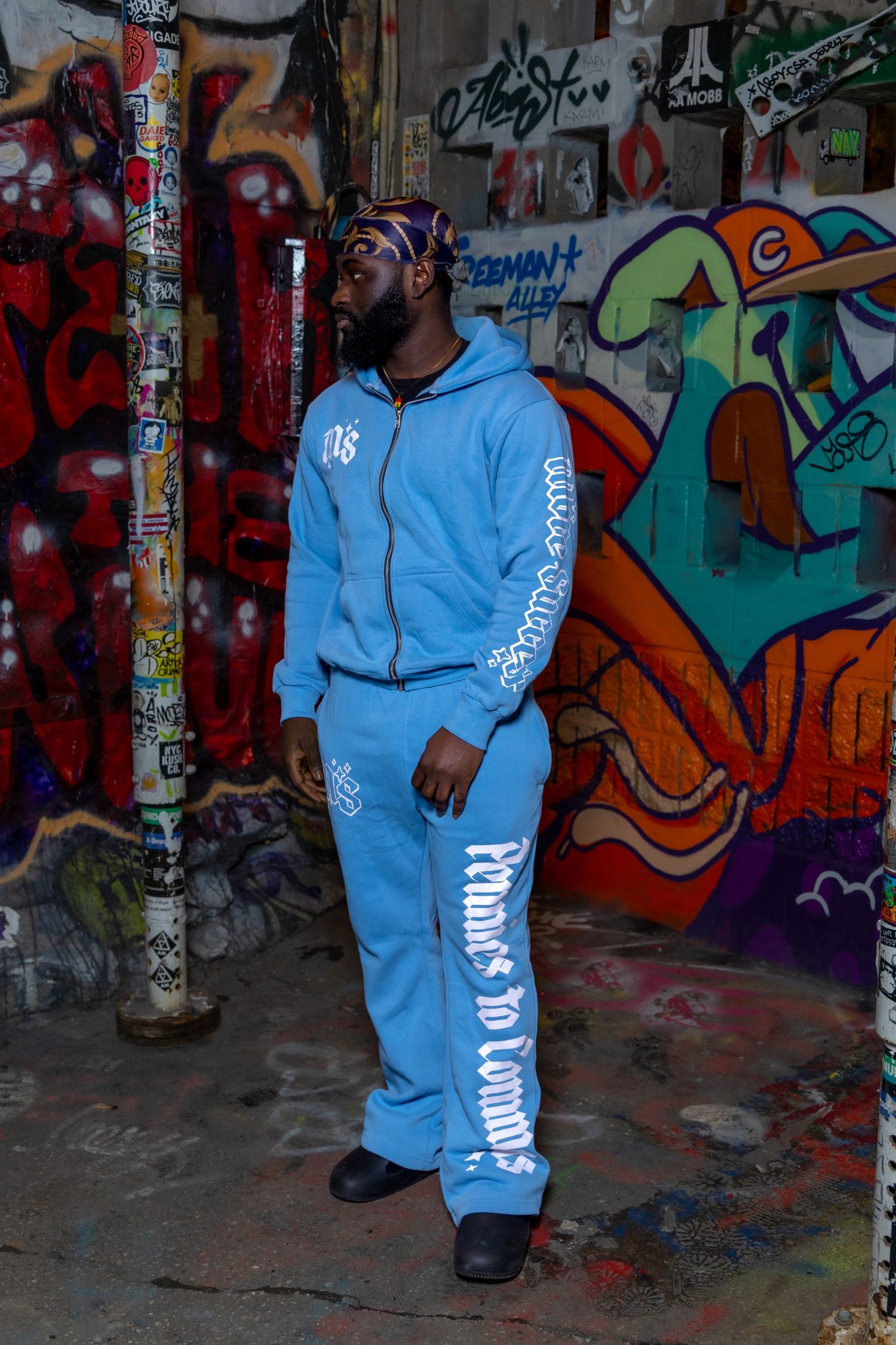 Light blue tracksuit ensemble photographed against graffiti wall backdrop.