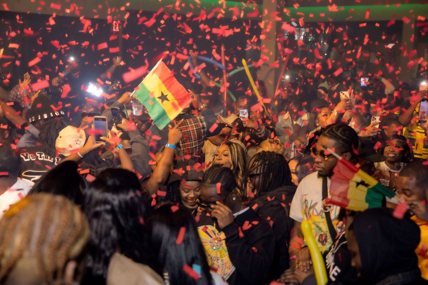Energetic crowd celebrating with Ghana flags and confetti at a nighttime event.