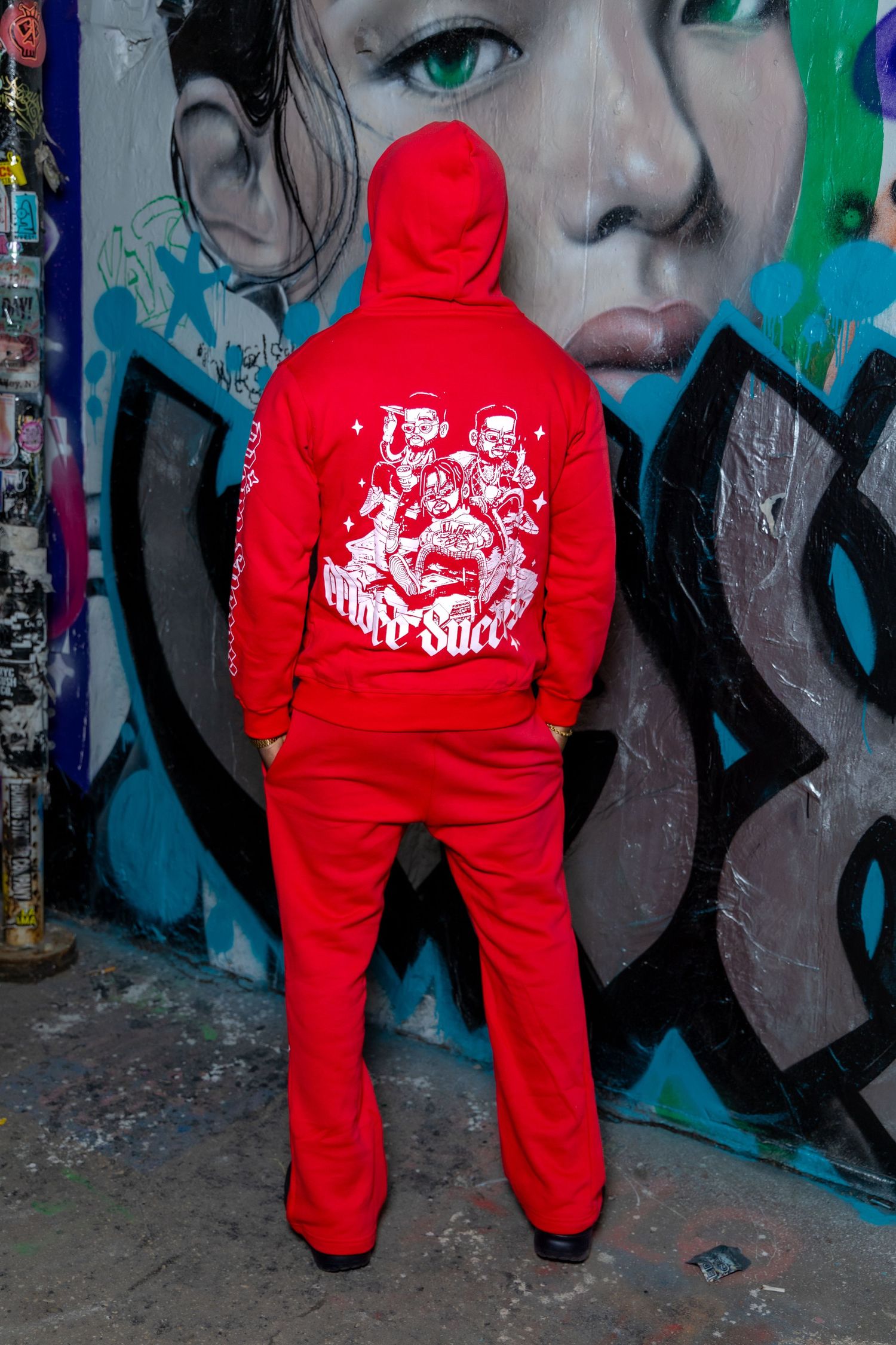 Back view of red tracksuit with graphic design hoodie against colorful street art wall.