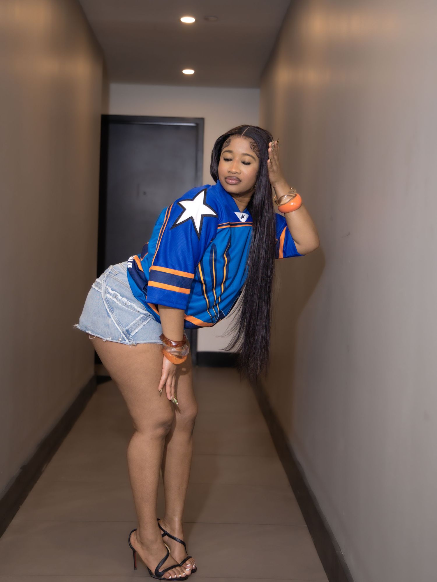 Person in blue jersey and denim shorts posing confidently in hallway.