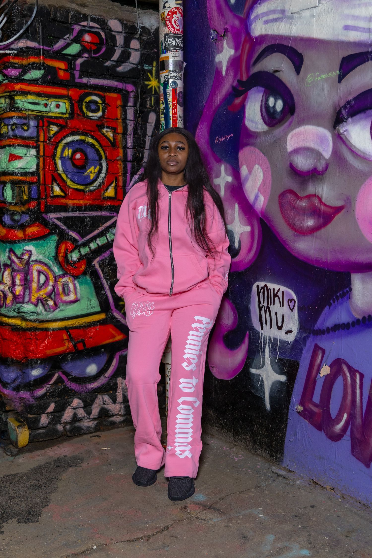 Streetwear photoshoot featuring pink tracksuit ensemble against urban art backdrop.