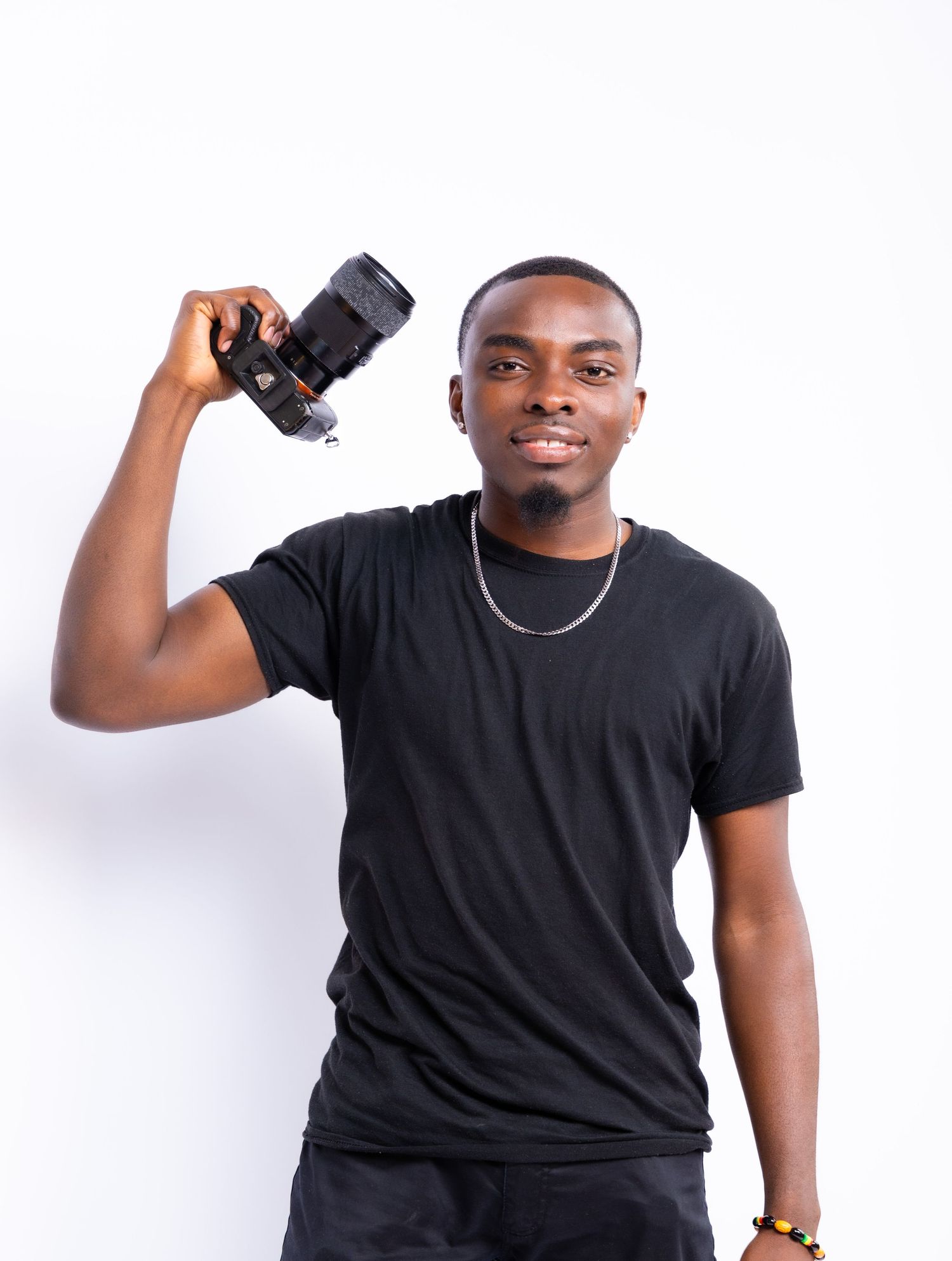 Photographer in black t-shirt holding camera while smiling against white background.