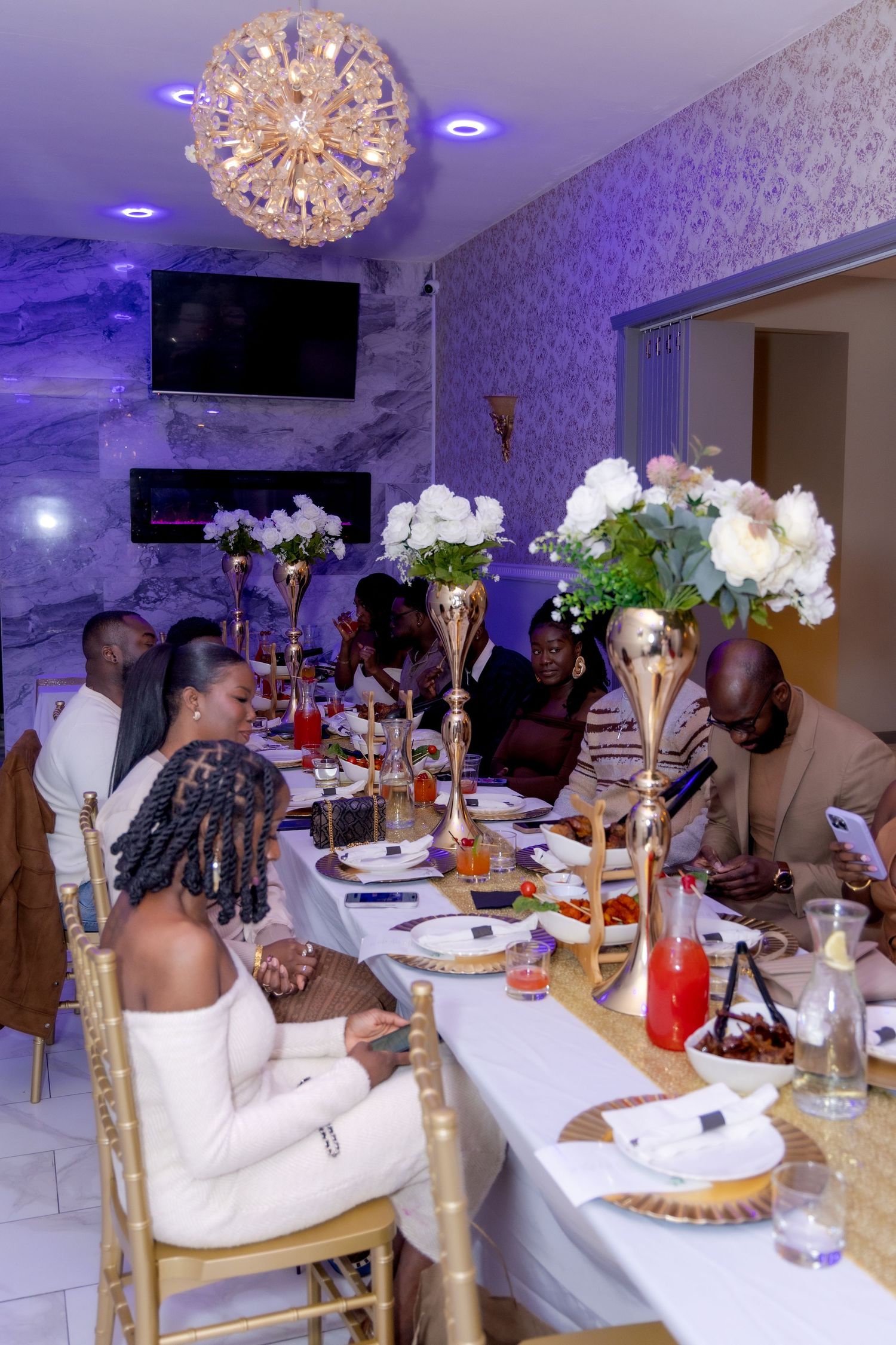 Elegant dinner party setting with crystal chandelier and floral centerpieces.