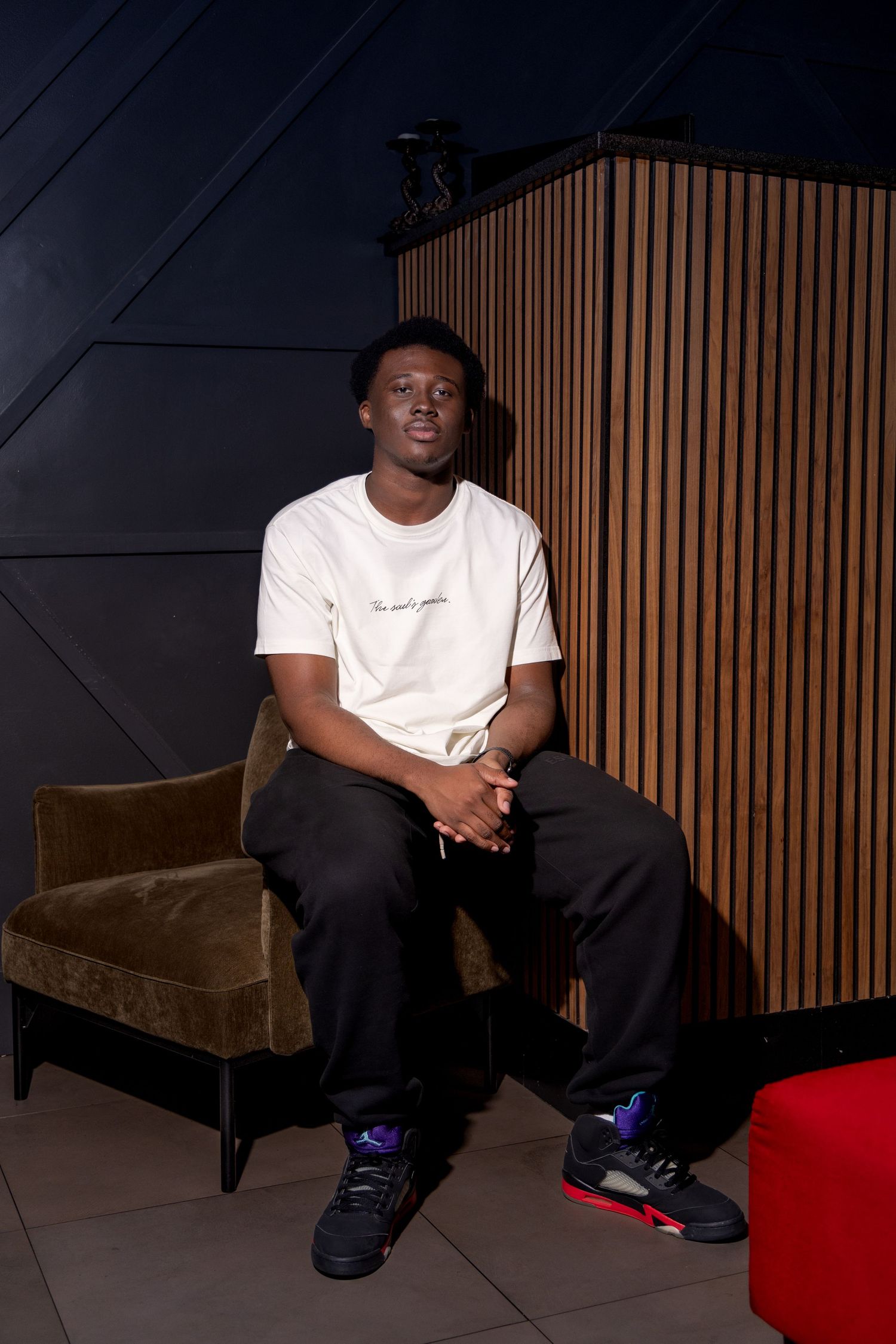 Person in white t-shirt and dark pants sitting casually on brown velvet couch.