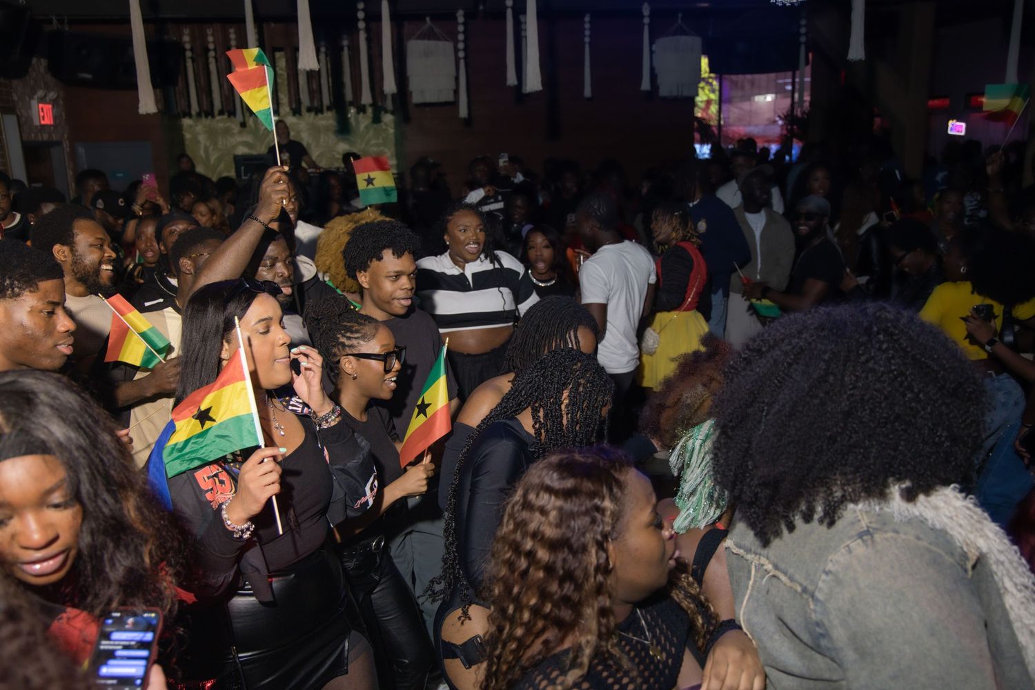 Festive crowd waving Ghana flags and celebrating at a nightclub party.