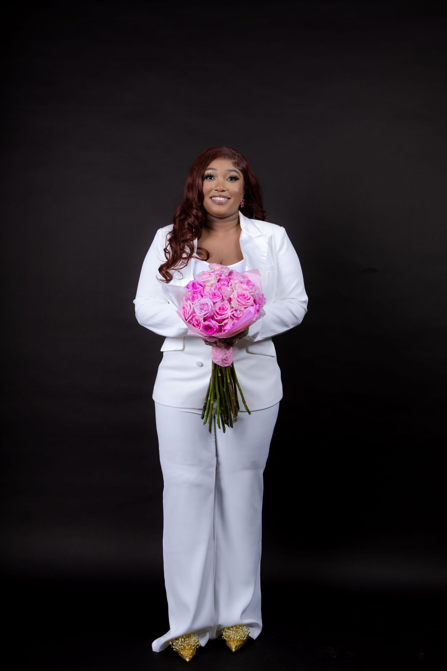 A woman in an all-white outfit holds a vibrant pink peony bouquet against a dark background.