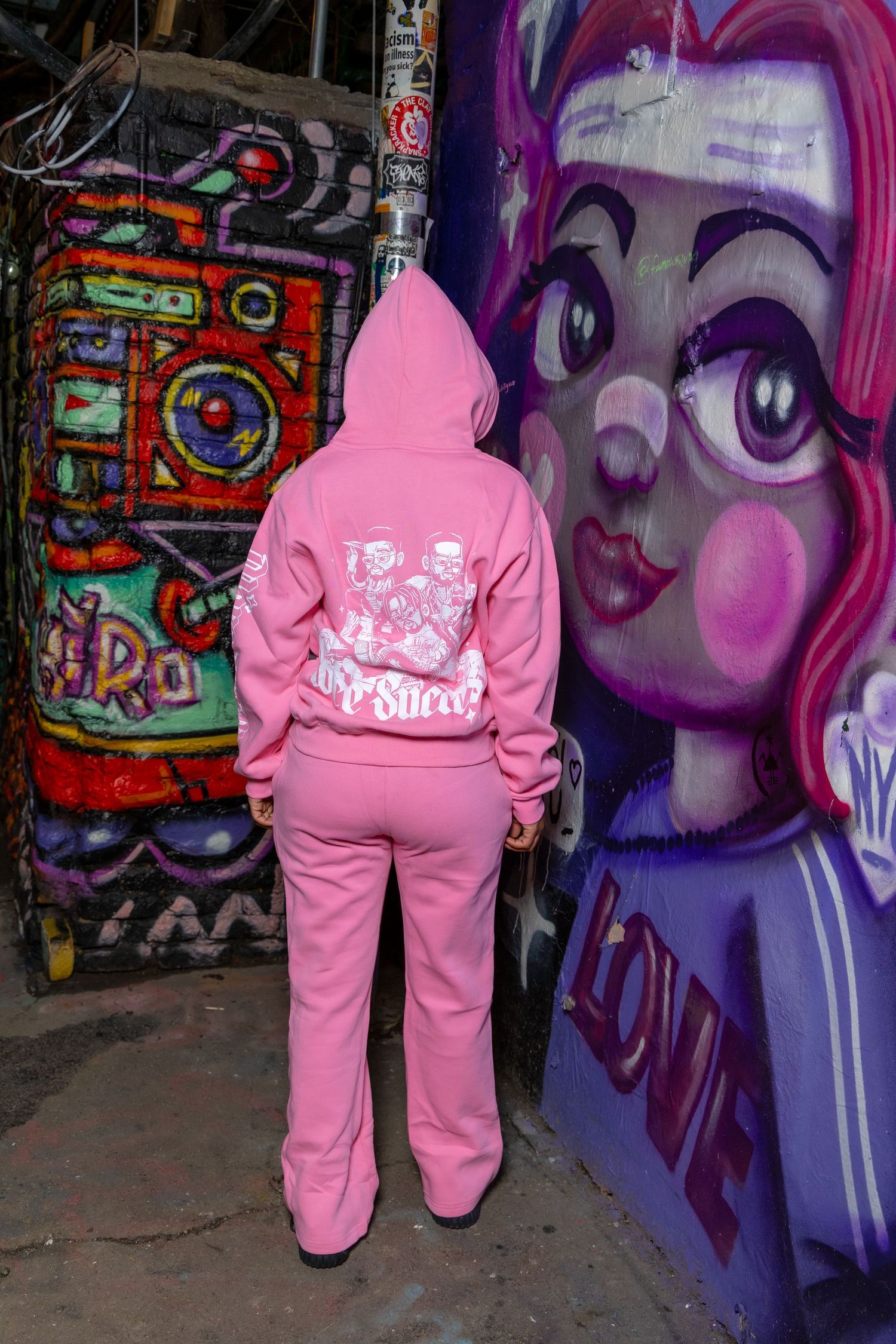 Back view of pink tracksuit with graphic print against graffiti art background.
