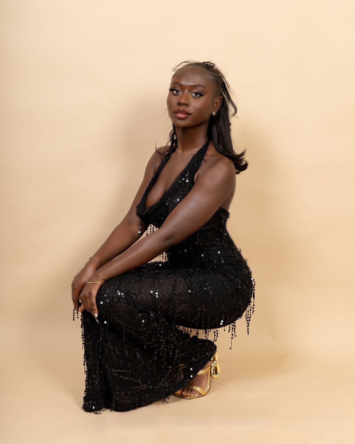 Model in a sequined black gown poses elegantly against a beige backdrop.