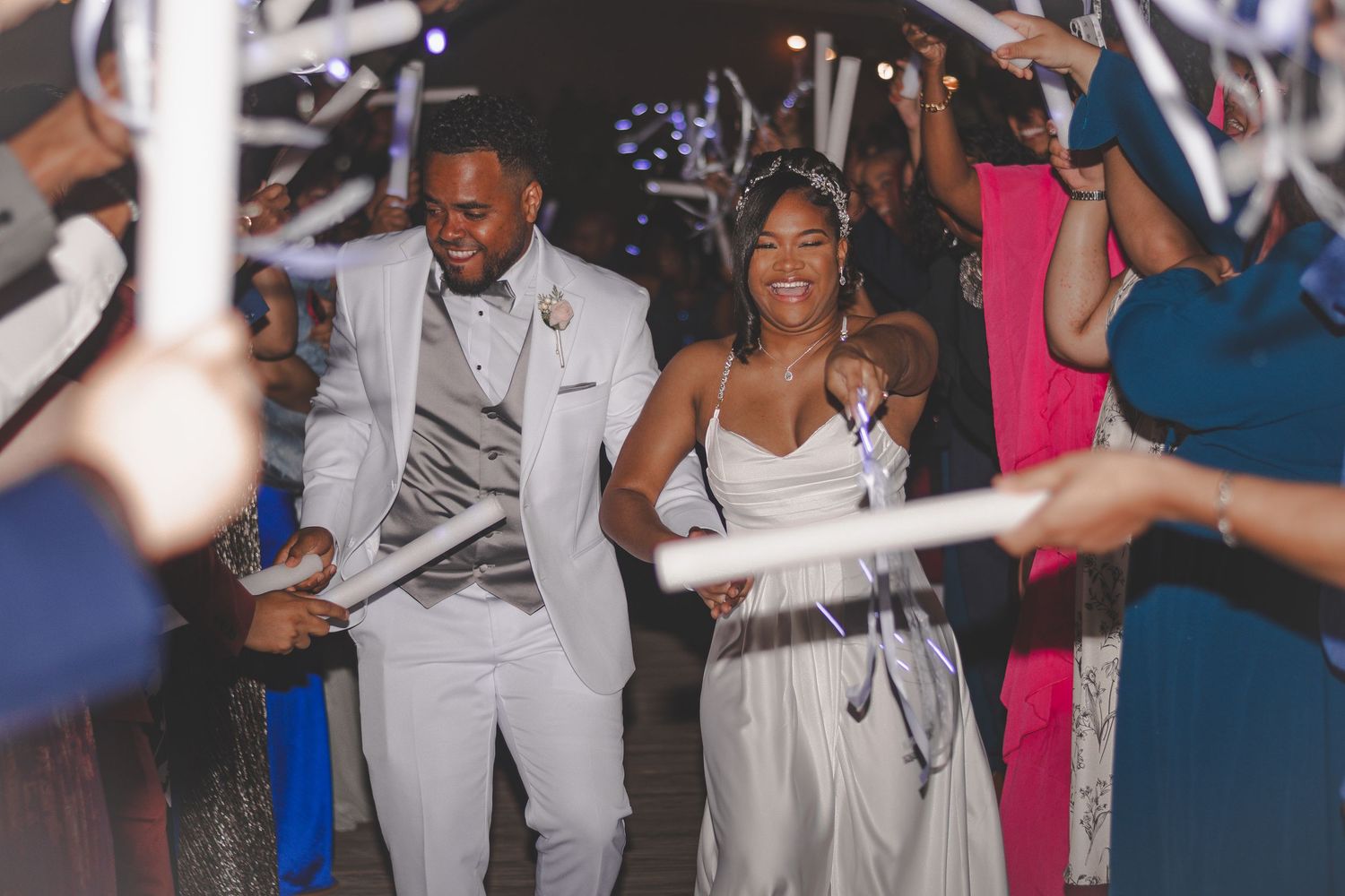 Wedding party members dance and celebrate at a reception with sparklers and colorful lighting.