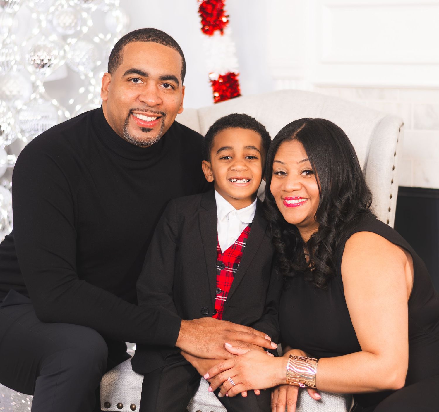 Family of three posing for a Christmas portrait, dressed in elegant black and red holiday attire.