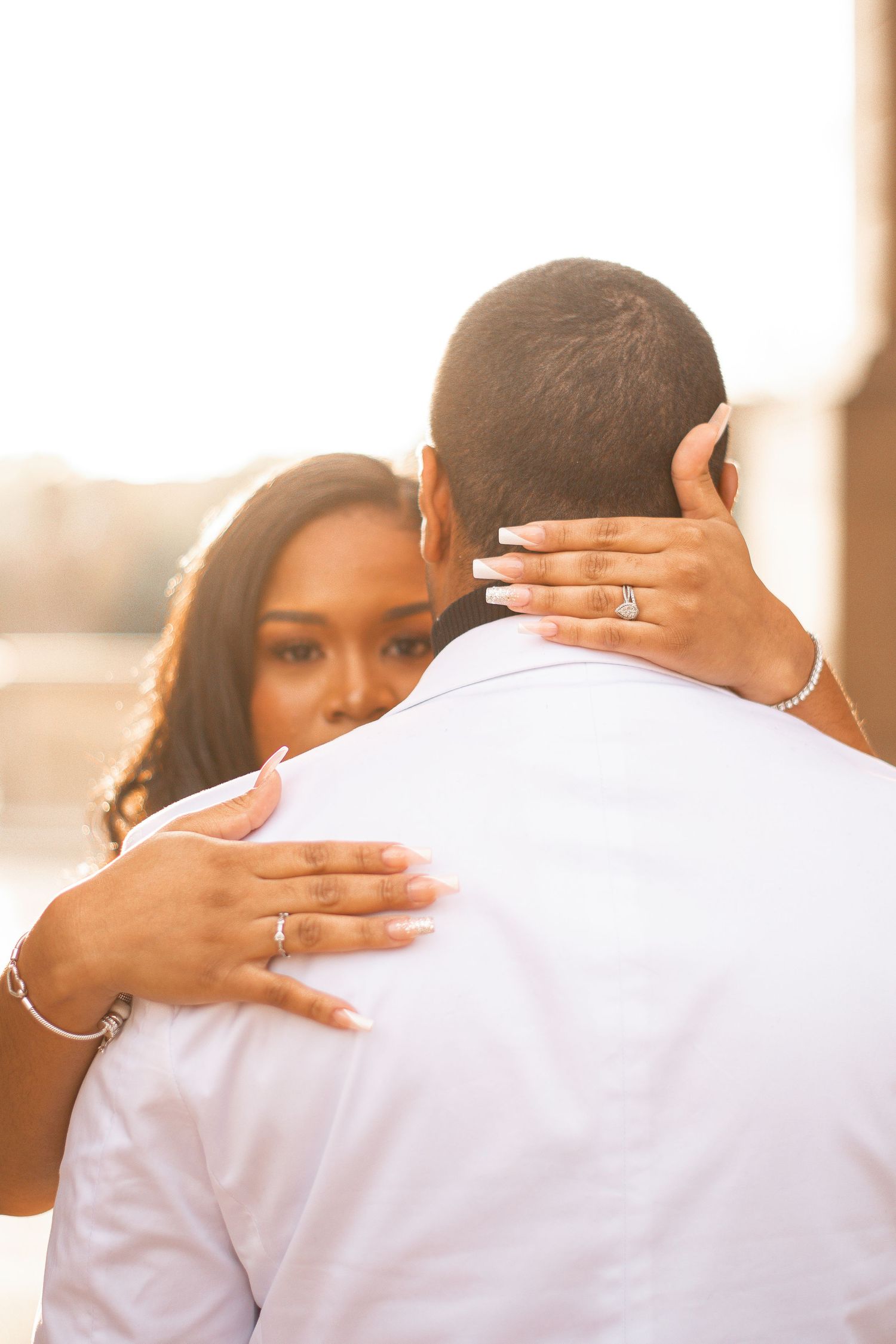 Intimate embrace showing hands with engagement ring during golden hour photoshoot.