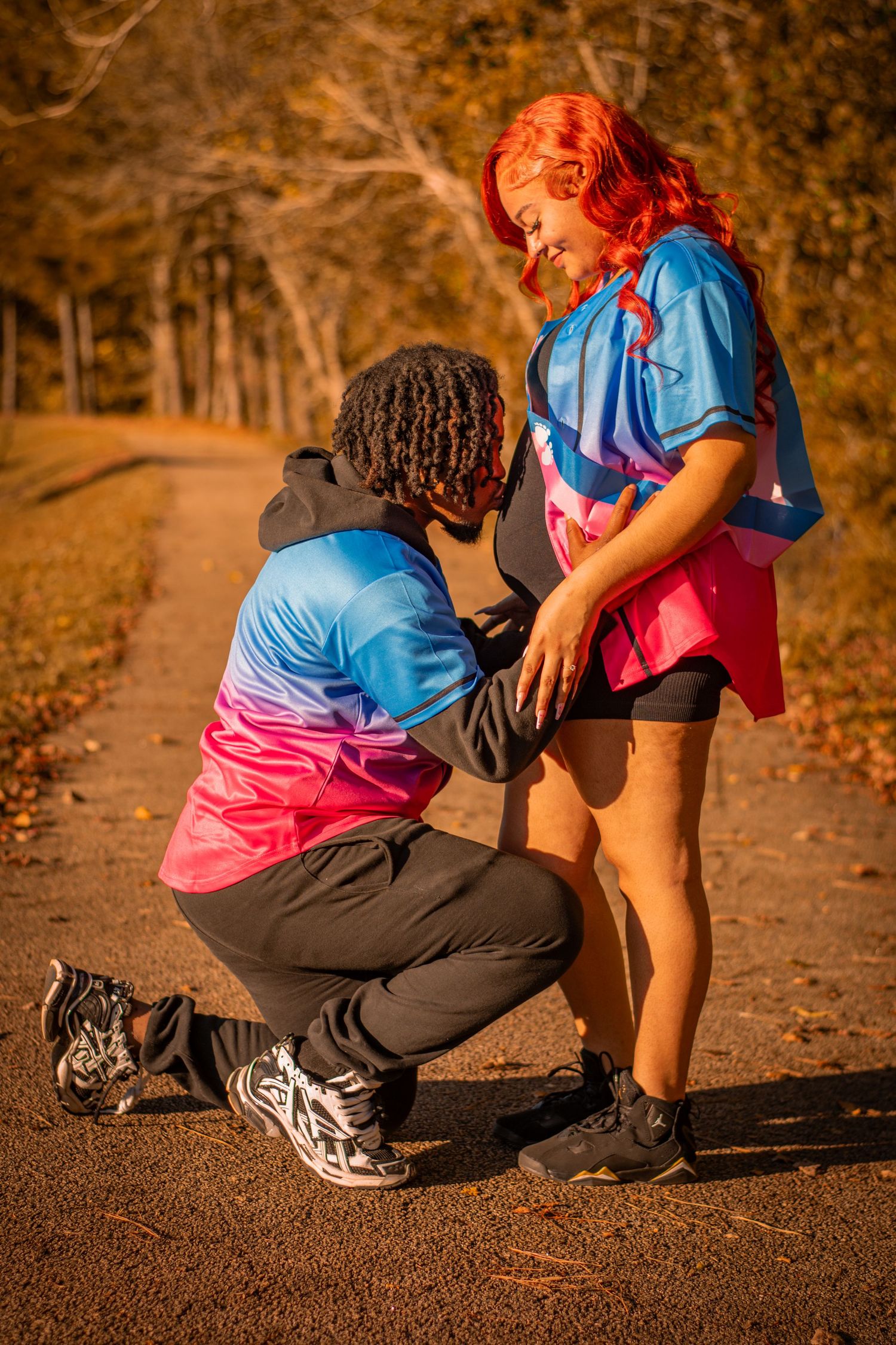 A romantic proposal scene on an autumn path with two people in matching blue and pink outfits.