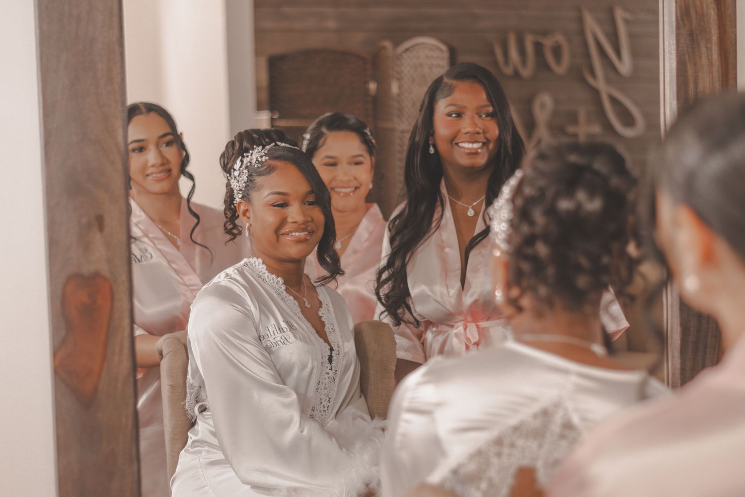 A group wearing white satin robes gather together smiling and laughing during a wedding preparation moment.