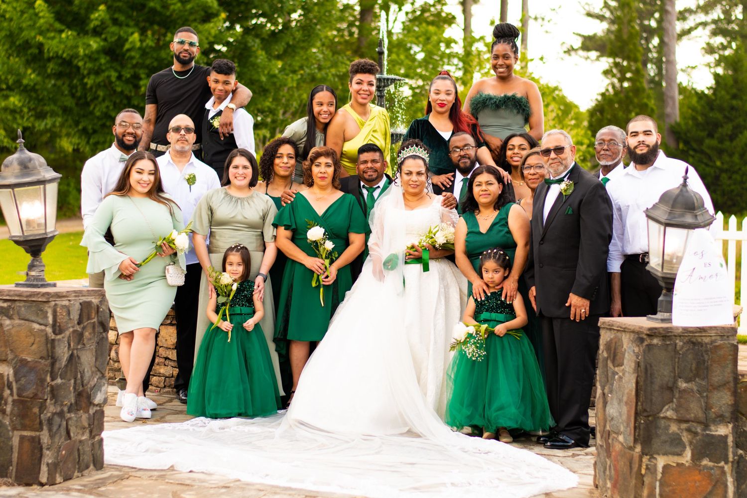 Wedding party in emerald green and white poses together on stone steps.