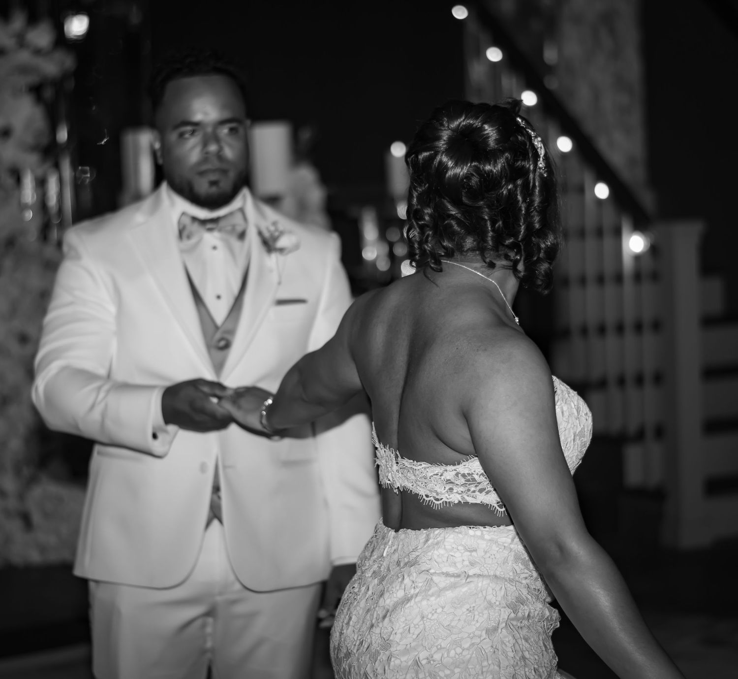 Black and white photo of a couple in formal wedding attire dancing together during a celebration in an elegant venue.