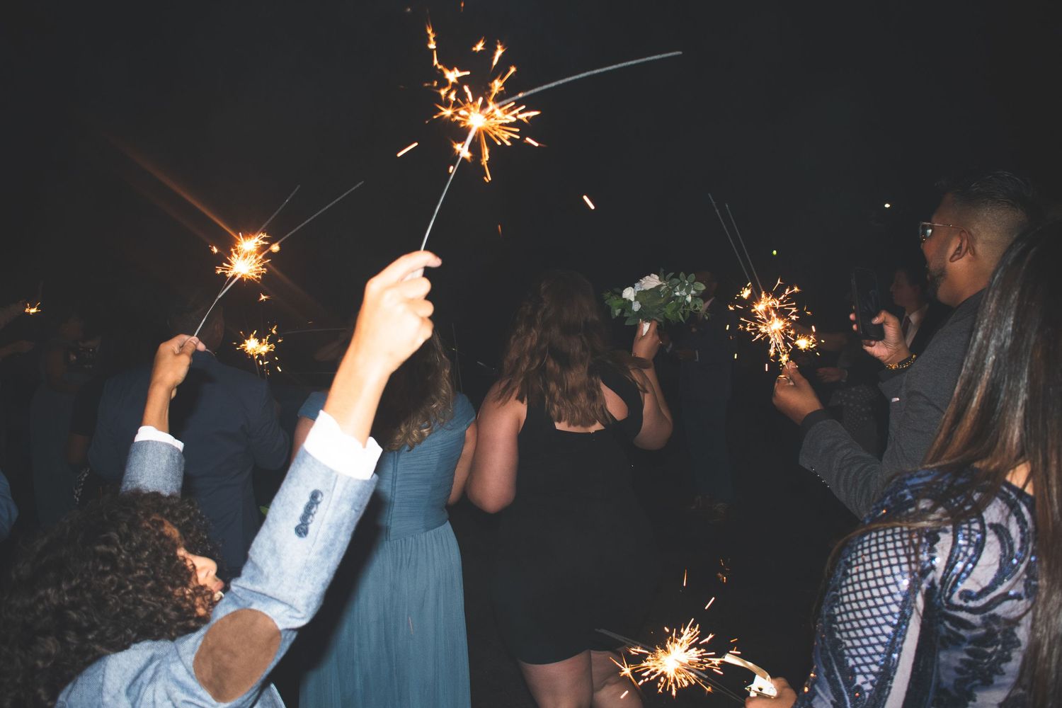 Group of people celebrating with sparklers at night in festive attire.