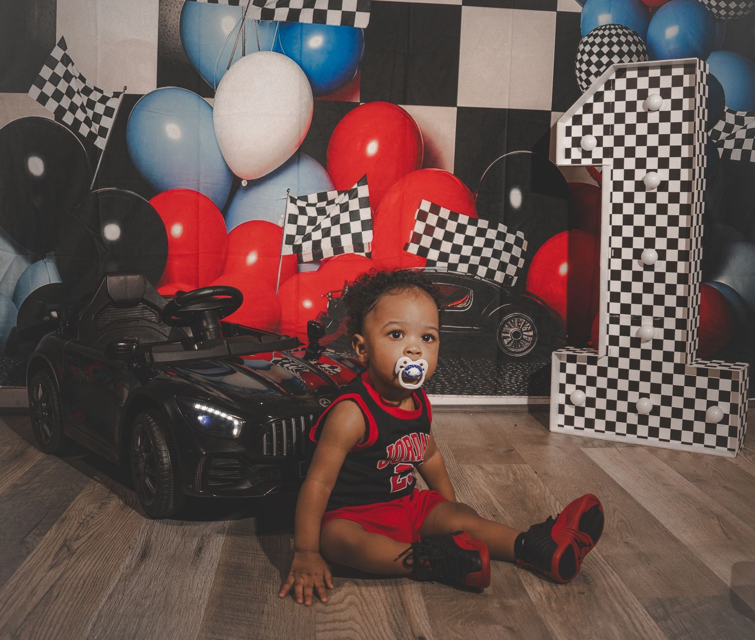 A racing-themed party setup with black and white checkered decorations, blue and red balloons against a decorated wall.