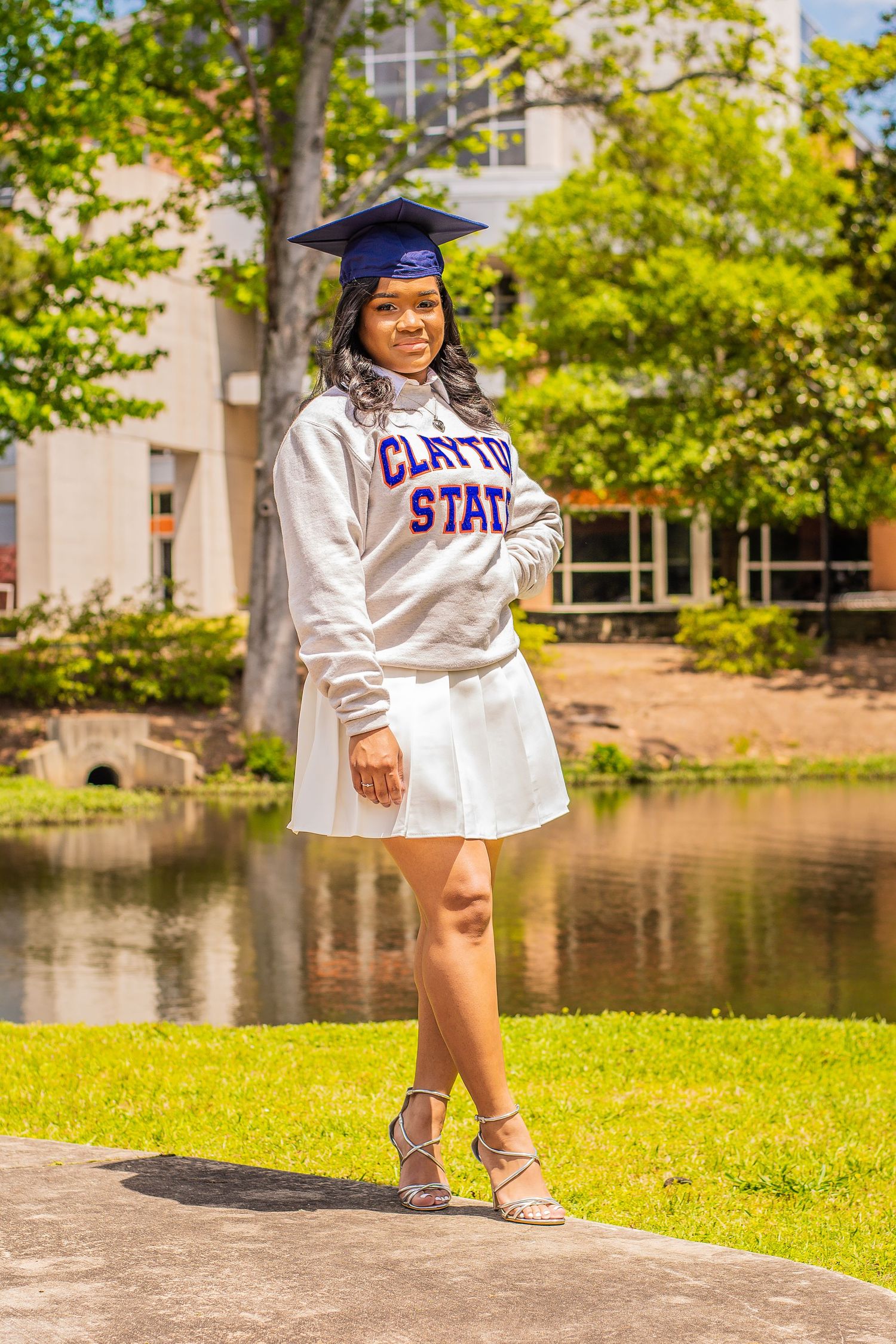 A graduate in Clayton State University attire poses by a lake on campus.